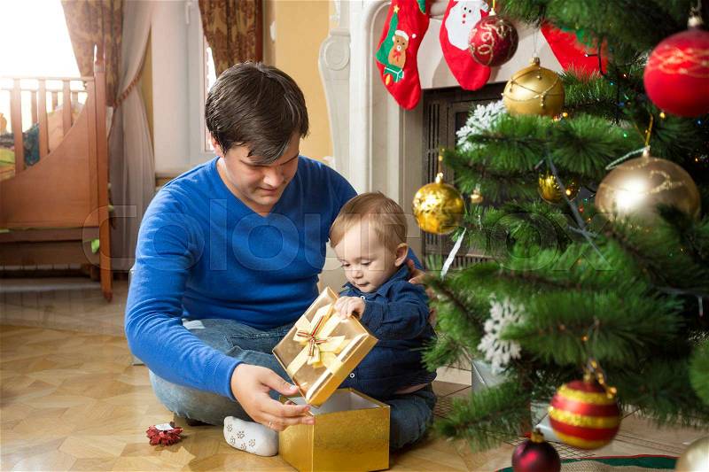 Young father and cute baby son opening Christmas gifts on floor, stock photo