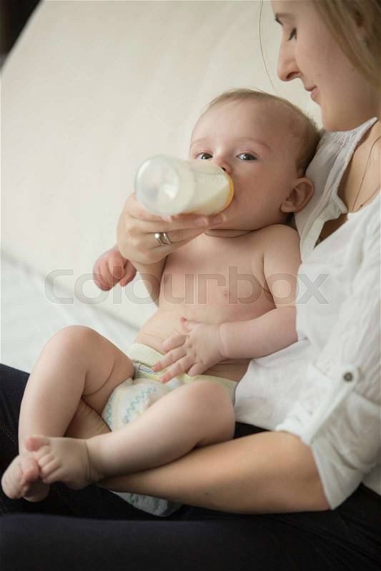 Beautiful young mother feeding with milk her cute baby boy, stock photo