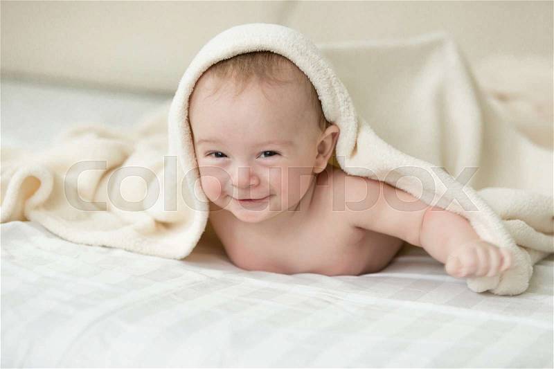 Cute cheerful baby lying under blanket on bed, stock photo