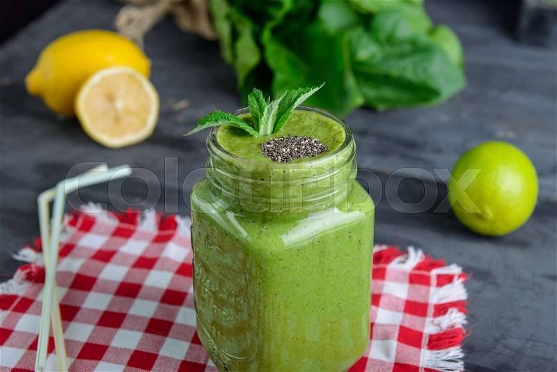 Healthy green spinach smoothie in a jar mug decorated with mint and chia seeds with ingredients on the checkered red napkin on the black wooden table. Selective focus, stock photo