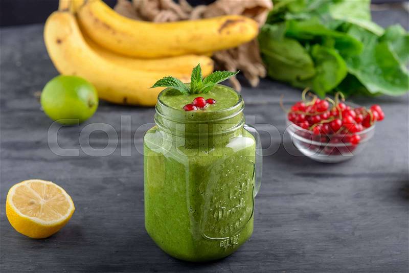 Healthy green spinach smoothie in a jar mug decorated with mint and red currant berries with ingredients on the black wooden table. Selective focus. Detox concept, stock photo