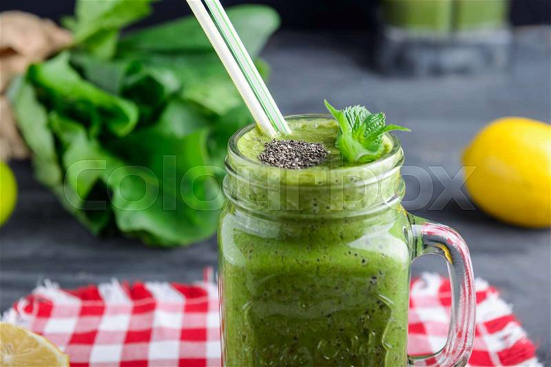 Healthy green spinach smoothie in a jar mug decorated with mint and chia seeds with ingredients on the checkered red napkin on the black wooden table. Selective focus, stock photo