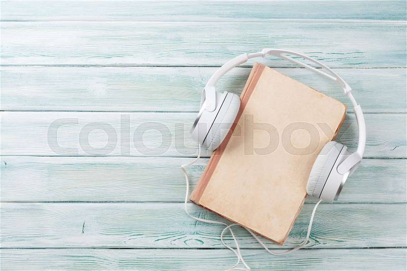 Audio book concept. Headphones and old book over wooden table. Top view with space for your text, stock photo