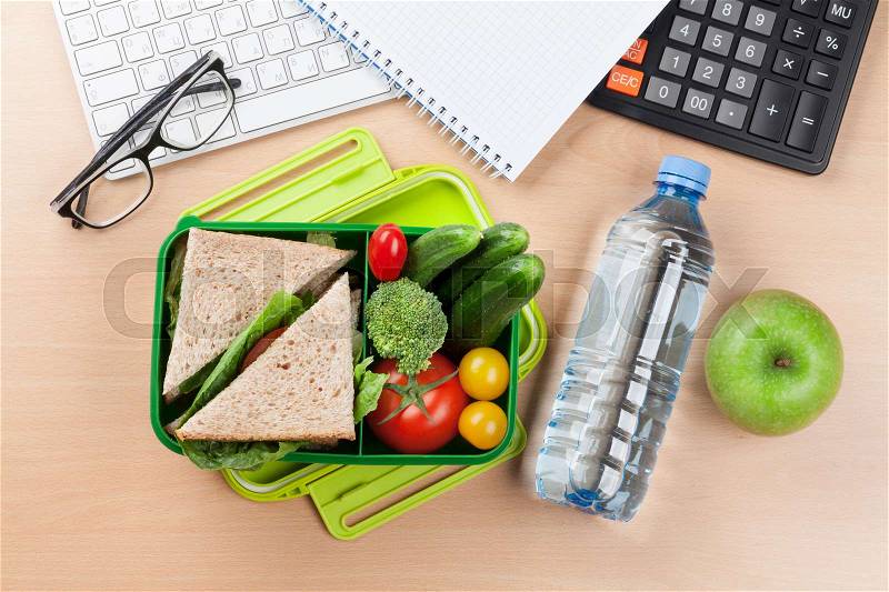 Office desk with supplies and lunch box with vegetables and sandwich. Top view, stock photo