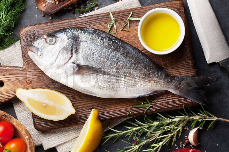 Raw fish cooking and ingredients. Dorado, lemon, herbs and spices. Top view on stone table, stock photo
