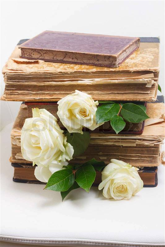 Old books pile with white rose flowers on white chair background, stock photo