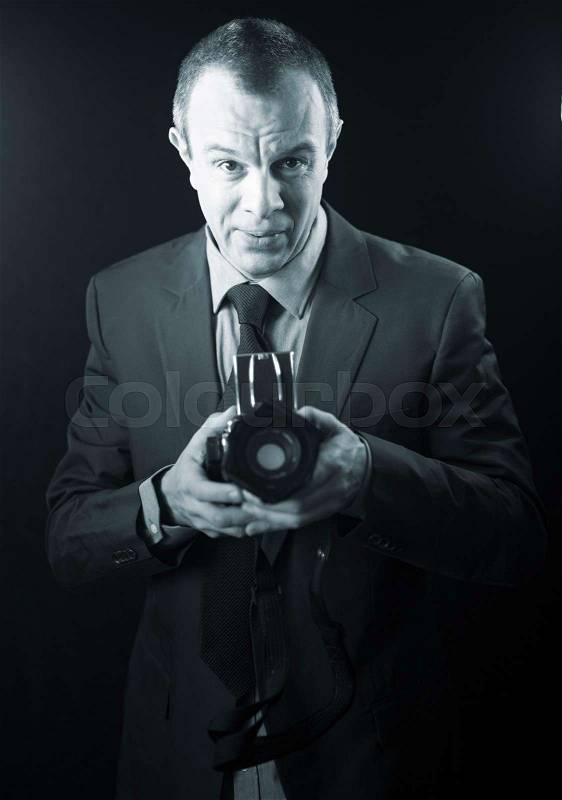 Photographer in studio in suit with camera aged in 40\'s against plain studio portrait background, stock photo