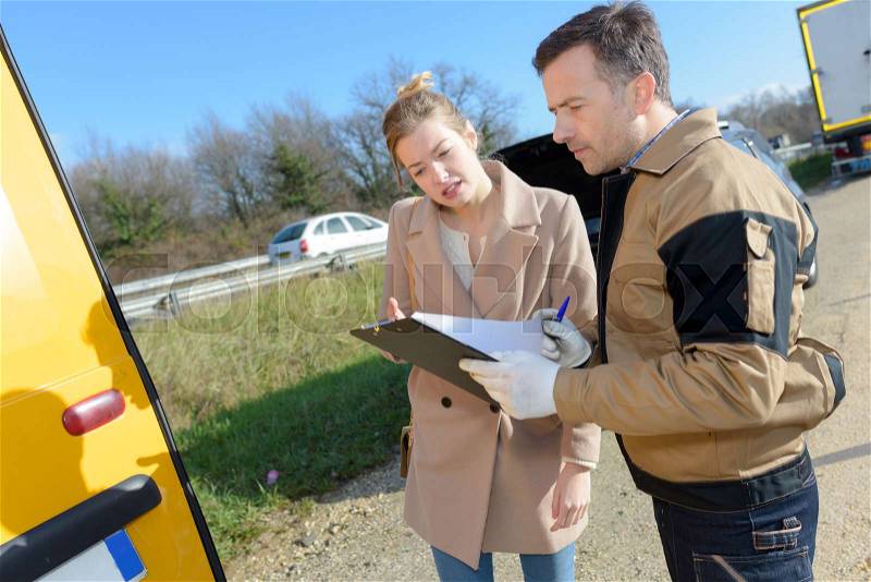Woman signing insurance paperwork after a car breakdown, stock photo