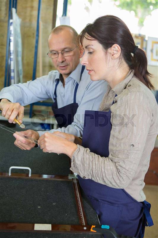 Senior shoemaker training apprentice to work with leather, stock photo