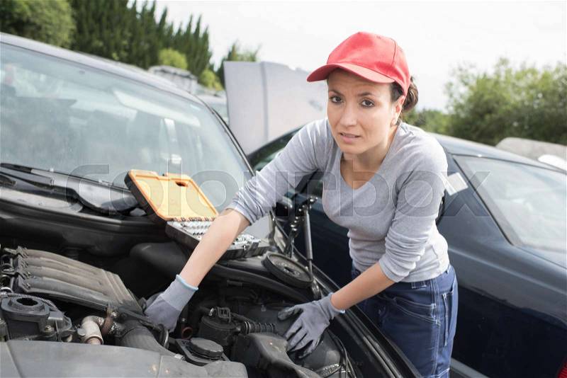 Beautiful mechanic woman working on a car, stock photo