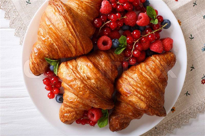 Golden croissants with fresh summer berries close-up on a plate. horizontal view from above , stock photo