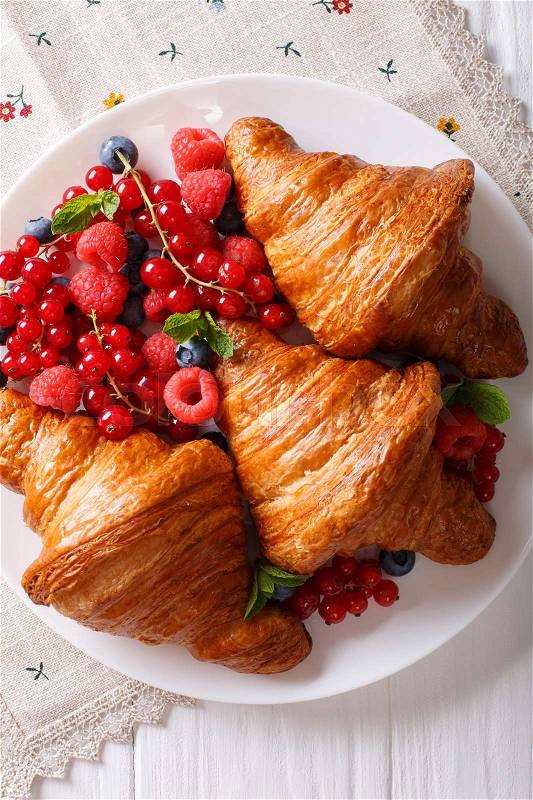 Golden croissants with fresh summer berries close-up on a plate. Vertical view from above , stock photo