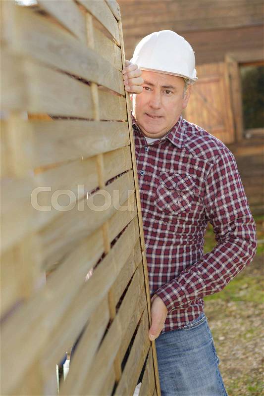 Senior construction worker carrying a framed interior wall, stock photo