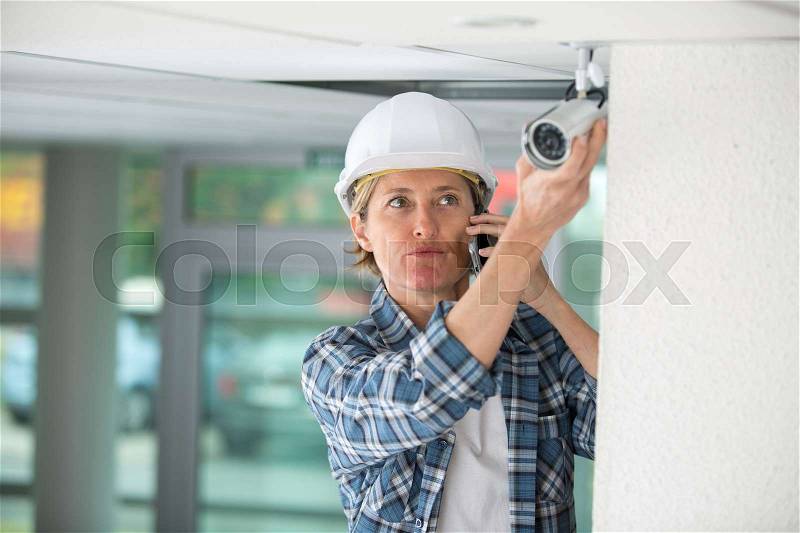 Worried female technician using the phone while installing camera, stock photo