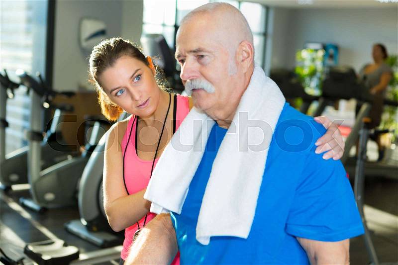 Young instructor with arm around senior man in sportswear, stock photo