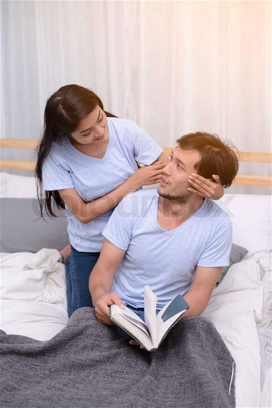 Couple play funny while reading a book together in bedroom, stock photo