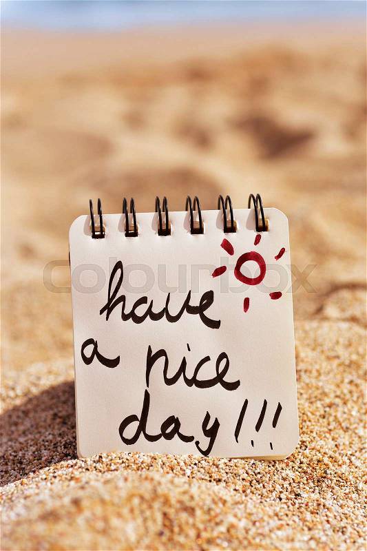 Closeup of a notepad with the text have a nice day written in it, placed on the sand of a beach, stock photo