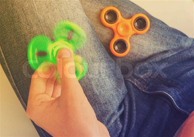 Trendy fidget spinner - person holding spinning fidget spinner in hand, close up view, retro toned, stock photo