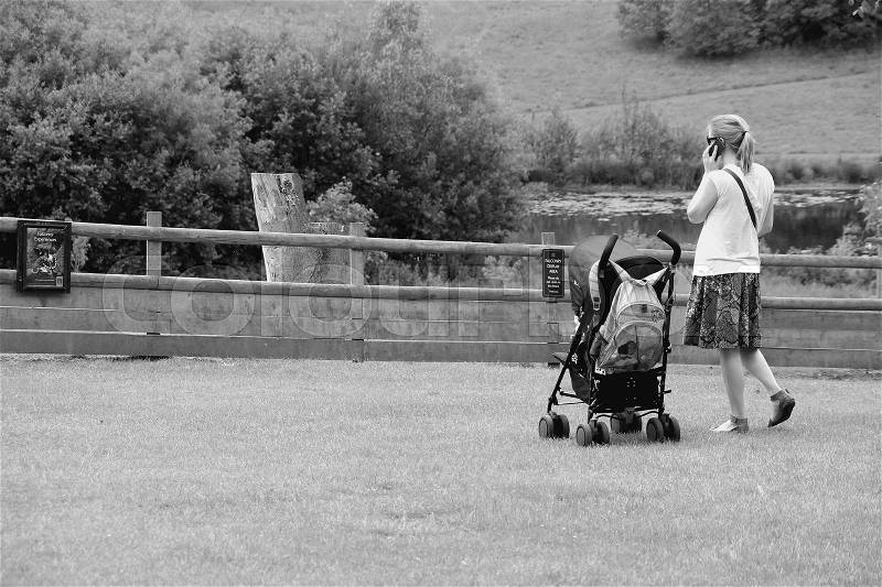 The lady is talking with her mobile phone in the park in Leeds Castle in Kent in England in the summer in black and white, stock photo