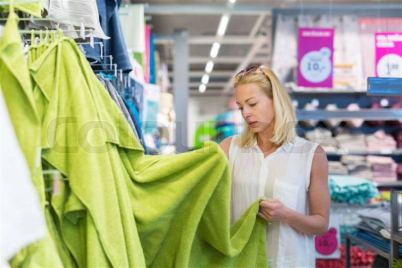 Pretty, young woman choosing the right towel for her apartment in a modern home decor furnishings store, stock photo
