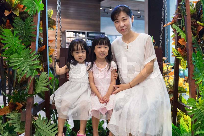 Asian Chinese mother and daughters sitting on a swing at indoor garden, stock photo