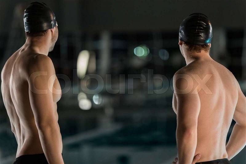 Rear view of two male swimmers with their hands on hips, stock photo