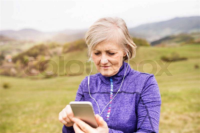 Active senior runner outside on green hills with smartphone and earphones, listening music. Banska Stiavnica, Slovakia, stock photo
