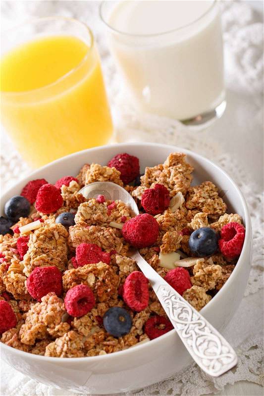Multigrain granola with dried raspberries, nuts and blueberries, milk and juice close-up on the table. vertical , stock photo