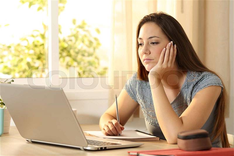 Serious student learning on line watching content in a laptop sitting in a table in her room at home, stock photo