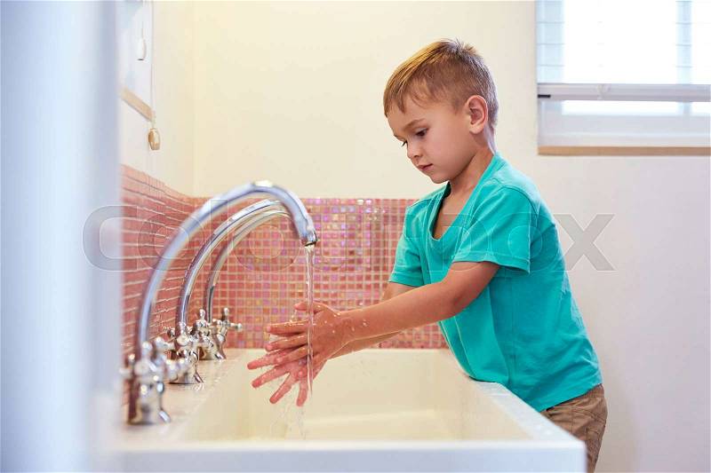 Male Pupil At Montessori School Washing Hands In Washroom, stock photo