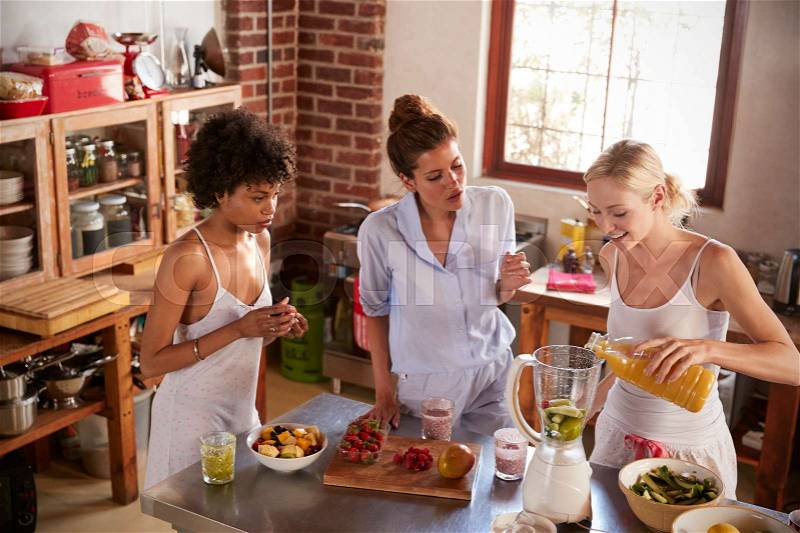 Three female friends making smoothies in kitchen, stock photo