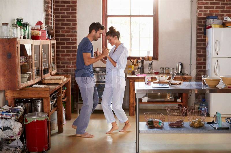 Hispanic couple in pyjamas dancing in kitchen, full length, stock photo
