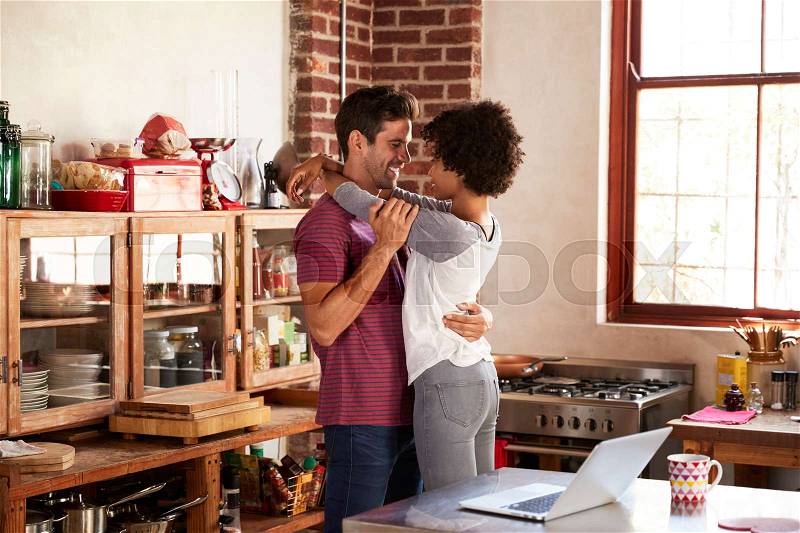 Young couple embracing in kitchen, three quarter length, stock photo