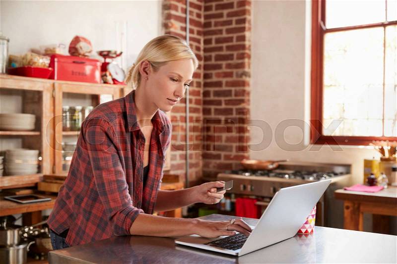 Young woman shopping on-line in her kitchen, waist up, stock photo