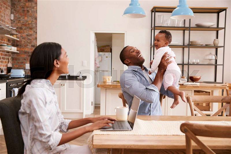 Mother Works From Home As Father Holds Baby Daughter, stock photo