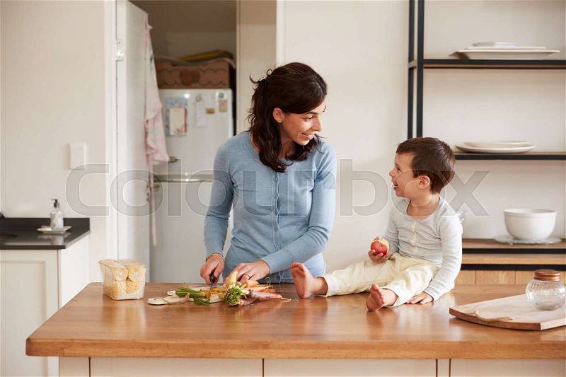 Son Helping Mother To Prepare Food On Kitchen Island, stock photo