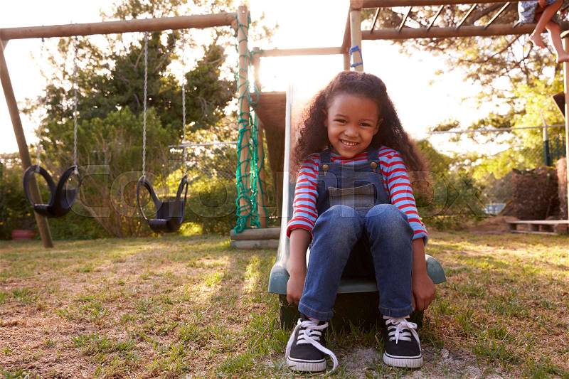 Portrait Of Girl Playing Outdoors At Home On Garden Slide, stock photo
