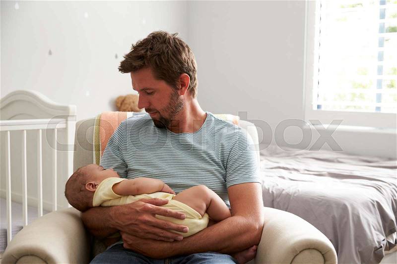 Father Sitting In Nursery Chair Holds Sleeping Baby Son, stock photo