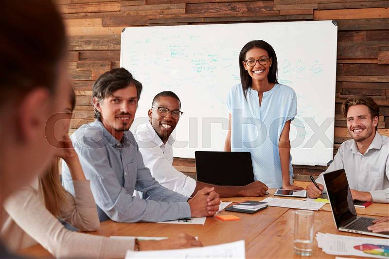 Young black woman and colleagues at meeting smile to camera, stock photo