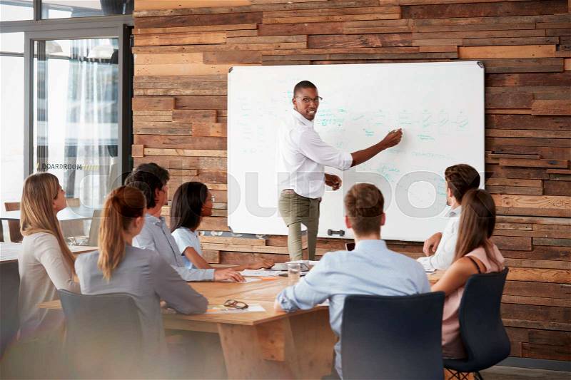 Young black man stands at whiteboard addressing team at meeting, stock photo