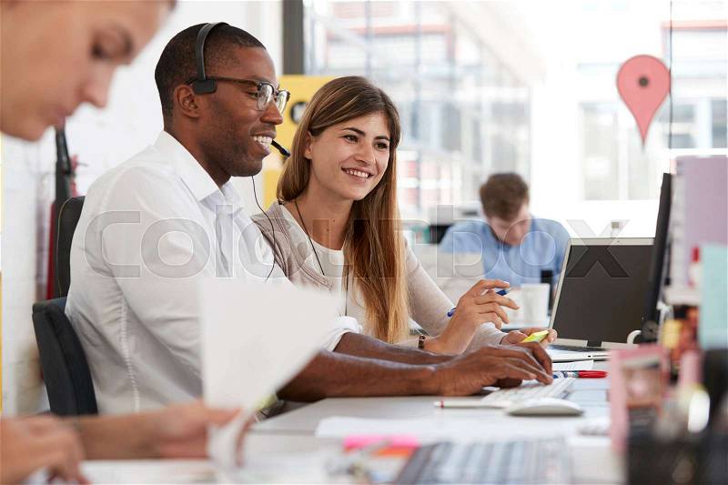 Young man and woman working with team in an open plan office, stock photo
