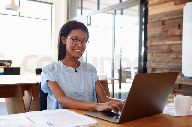 Young black woman using laptop in office smiling to camera, stock photo