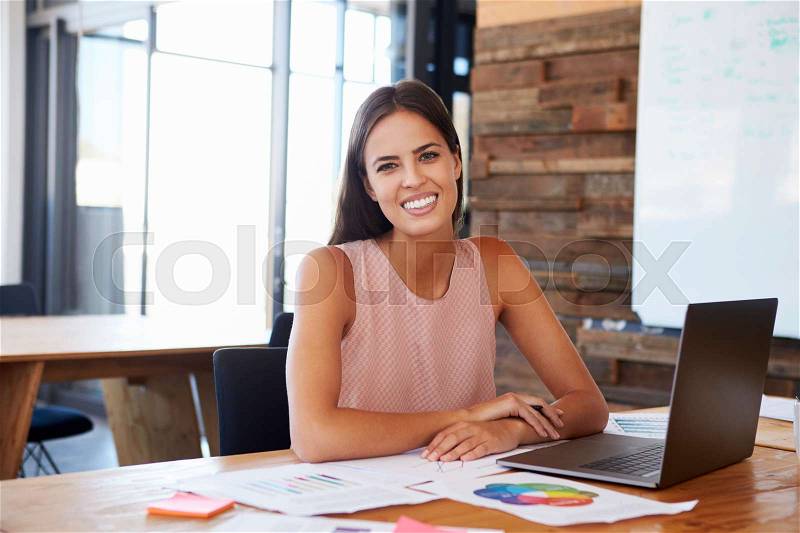 Woman in office using laptop smiles to camera, front view, stock photo