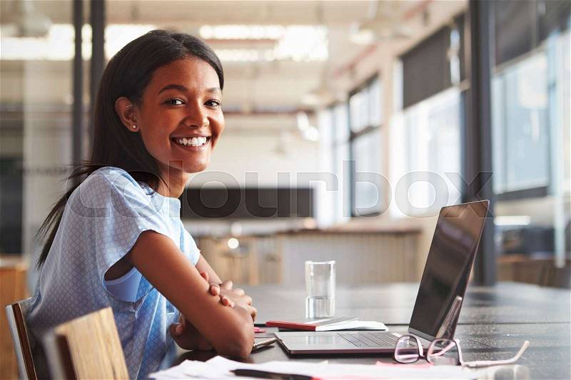 Young black woman in office using laptop smiling to camera, stock photo