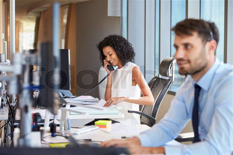 Businesswoman On Phone At Desk In Busy Office, stock photo