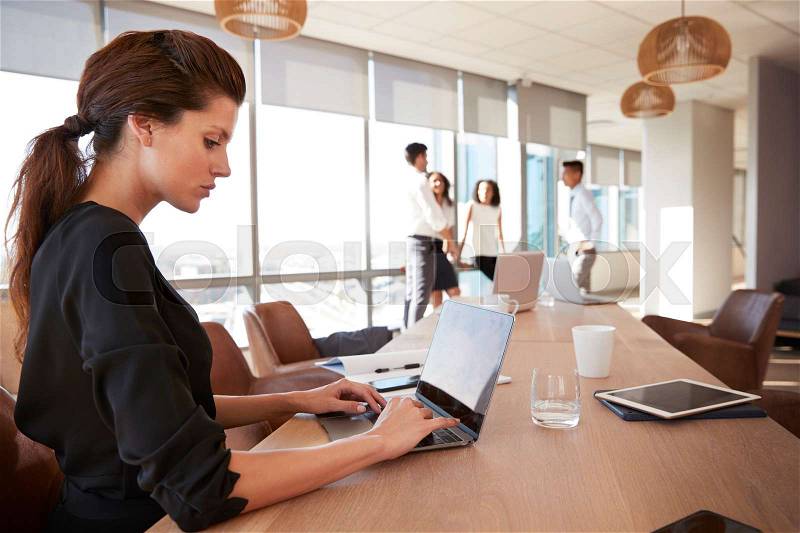 Businesswoman Uses Laptop As Colleagues Meet In Background, stock photo