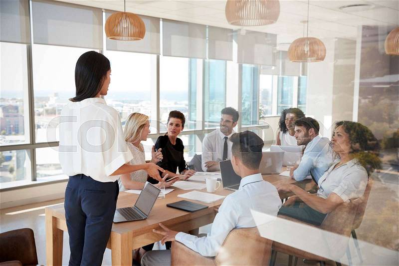 Businesswoman Leads Meeting Around Table Shot Through Door, stock photo