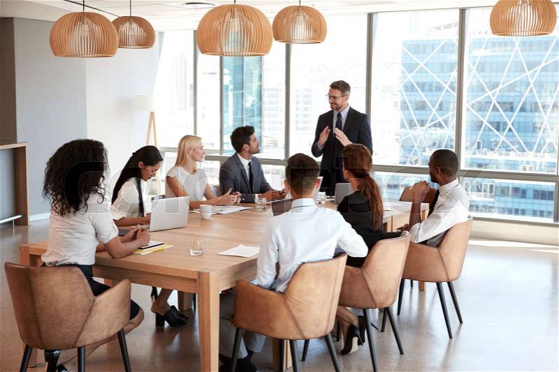 Businessman Stands To Address Meeting Around Board Table, stock photo