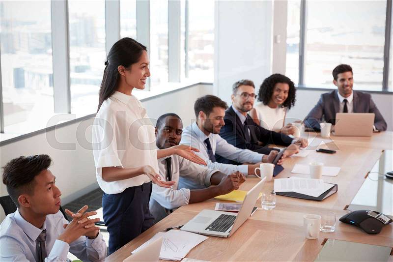 Businesswoman Stands To Address Meeting Around Board Table, stock photo