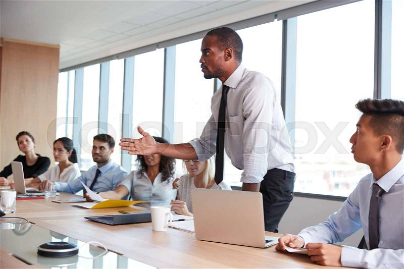 Businessman Stands To Address Meeting Around Board Table, stock photo